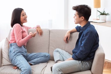 Asyalı çift, evdeki koltukta oturup sohbet etmekten keyif alıyor.