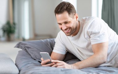 Akıllı telefon kullanan neşeli adam. Yatak odasında uzanıyor.