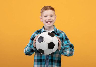 Sarı stüdyo arka planında futbol topuyla poz veren çocuk