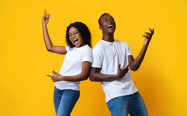 Homem negro alegre e mulher dançando e cantando em amarelo — Fotografia de Stock