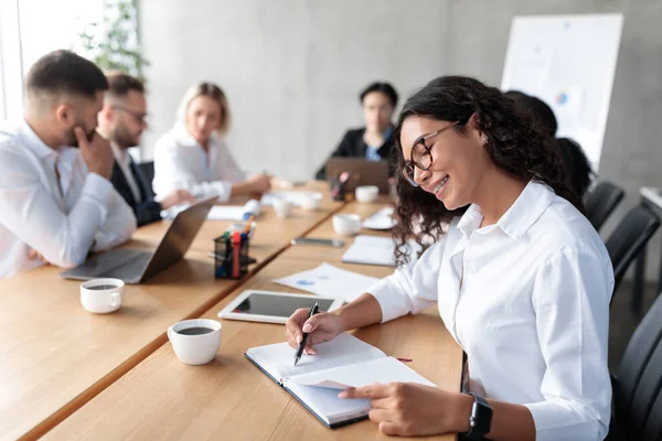 Empresaria tomando notas sentada en una reunión de negocios en una oficina moderna —  Fotos de Stock