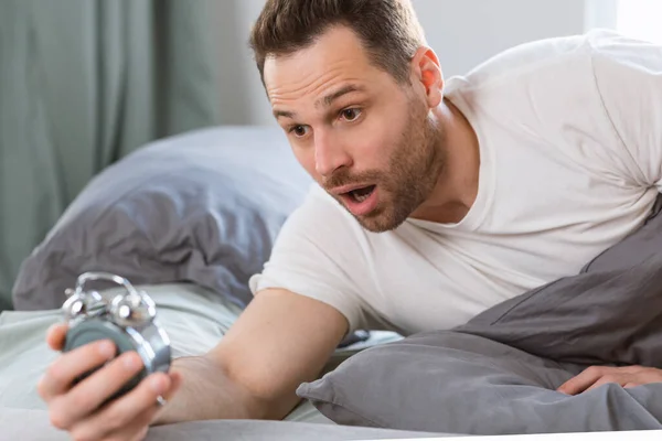 Șocat Overslept Guy Holding Ceas deșteptător minciună în pat — Fotografie, imagine de stoc