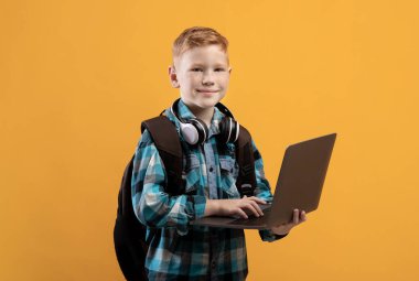 Sırt çantalı, kulaklıklı, dizüstü bilgisayarı olan neşeli okul çocuğu.