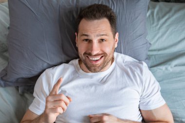 Yatakta uzanmış parmağını işaret eden bir adam, üst görünüm.