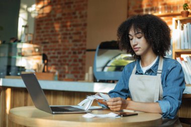 Önlüklü ciddi Afrikalı Amerikalı bayan barmen mali hesaplar ve muhasebe ile çalışıyor.