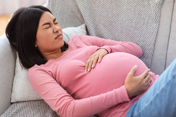Беременная китаянка страдает от боли, касающейся живота дома — стоковое фото
