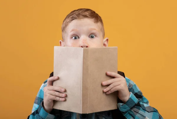 Шокированный мальчик, закрывающий рот книгой — стоковое фото