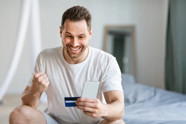 Joyful Man tenant Smartphone carte de crédit Gesturing Oui à la maison — Photo
