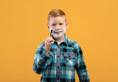 Oyuncu küçük çocuk sarı arka planda yüzünü tıraş ediyor.