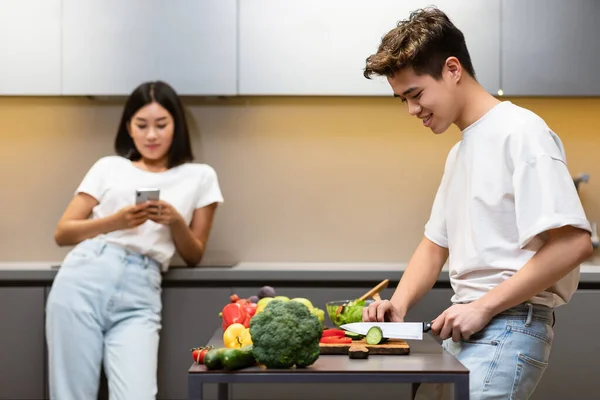 Asian Husband Cooking While Wife Texting On Phone In Kitchen — Stock Photo, Image