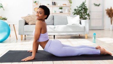 Evdeki spor minderinde yoga yapan, kobra pozu veren zinde bir zenci kadın.
