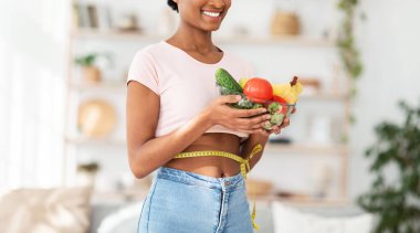 Kilo vermek için sağlıklı beslenme. Elinde mezura olan zenci kadın elinde meyve ve sebze kasesi tutuyor, yakın plan.