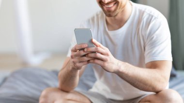 Yatak odasında cep telefonu ile telefon kullanan tanınmayan adam, kesilmiş.