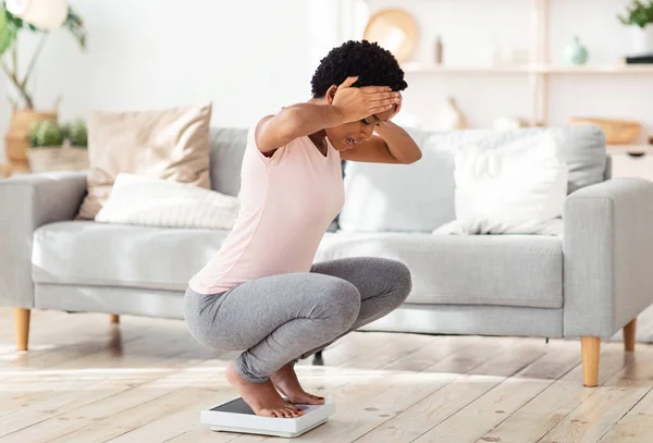 Jeune femme noire assise sur des échelles, choquée par la prise de poids à la maison, espace libre — Photo