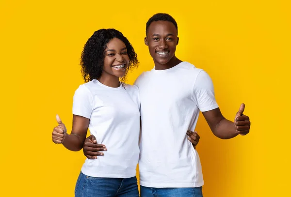 Felices amantes negros abrazándose y mostrando el pulgar hacia arriba en amarillo — Foto de Stock