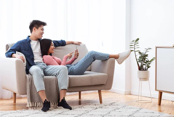 Casal asiático usando smartphone sentado no sofá em casa — Fotografia de Stock