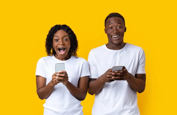 Hombre y mujer afroamericanos asombrados sosteniendo teléfonos inteligentes —  Fotos de Stock