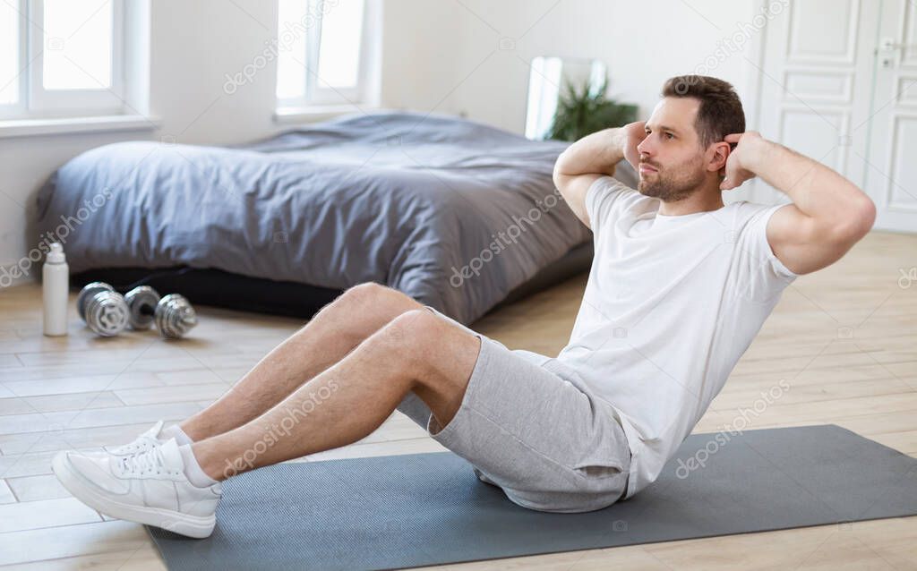 Sporty Man Doing Sit-Ups Abs Exercise On Mat In Bedroom