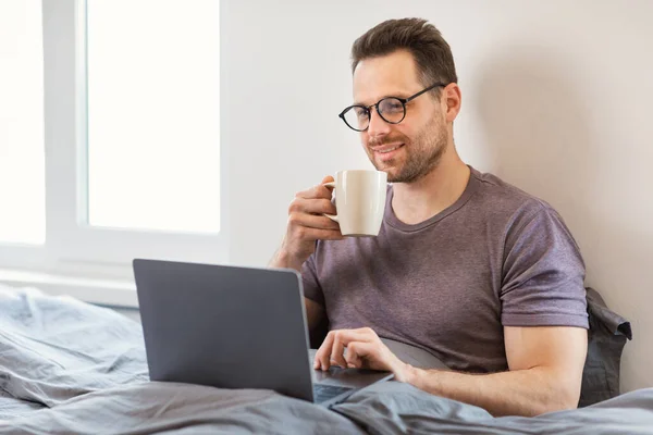 Человек сидит с ноутбуком компьютер в спальне смотреть фильм онлайн — стоковое фото