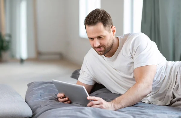 Человек с помощью планшета лежа в постели смотреть фильм онлайн в помещении — стоковое фото