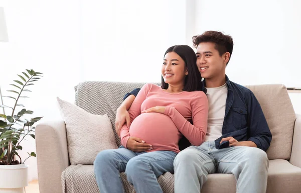 Asiático pareja viendo televisión esperando bebé sentado en casa —  Fotos de Stock