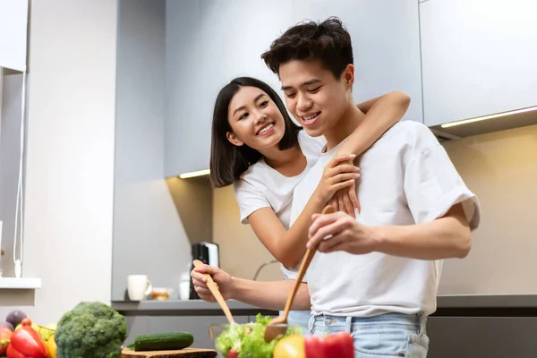 Asiatique femme étreignant mari tandis qu'il cuisine dîner dans cuisine — Photo