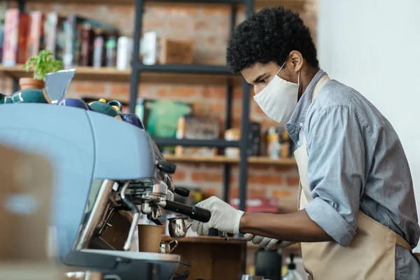 Millennial Africano americano barista com avental, máscara protetora e luvas faz take-out latte para o cliente — Fotografia de Stock