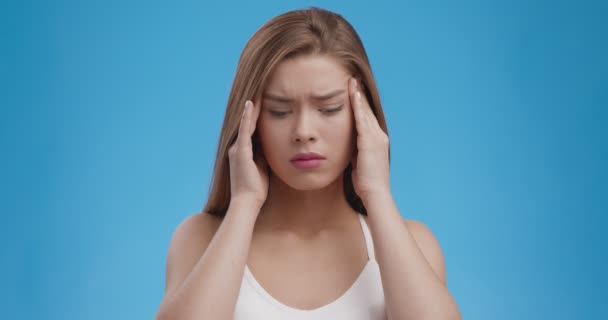 Migraine aanval. jong lijden aan hoofdpijn dame masseren haar tempels, blauwe studio achtergrond — Stockvideo