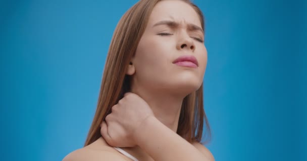 Jovem caucasiana sofrendo de dor aguda no pescoço, massagear e esticar os músculos doloridos, fundo azul — Vídeo de Stock