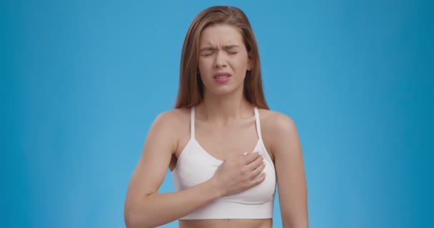 Kalp krizi tehdidi. Beyaz kadın göğsünde güçlü bir ağrı hissediyor, mavi arka plan — Stok video