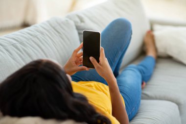 Evdeki rahat koltukta cep telefonu kullanan tanınmayan siyahi kadın, ekranda mobil uygulama tasarımı için model.