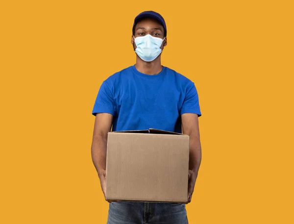 Zwarte bezorger in medisch masker met kartonnen doos — Stockfoto