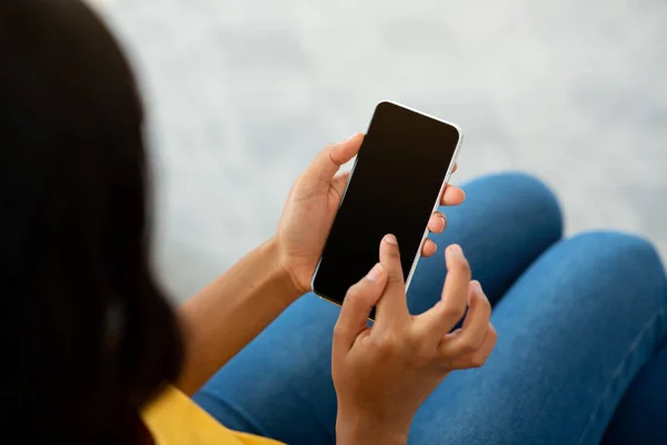 Нерозпізнавана чорна жінка використовує мобільний телефон з порожнім екраном в приміщенні, макет для мобільного додатку або дизайну веб-сайту — стокове фото