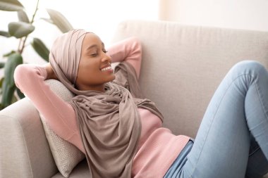 Güzel siyah kadın tesettürde uzanıyor, gözlerini kapıyor ve gülümsüyor, öğlen uyukluyor, evde.