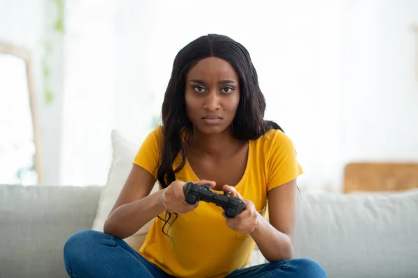 Restez à la maison passe temps. Dame noire sérieuse avec joystick jouer jeu vidéo sur canapé à l'intérieur — Photo