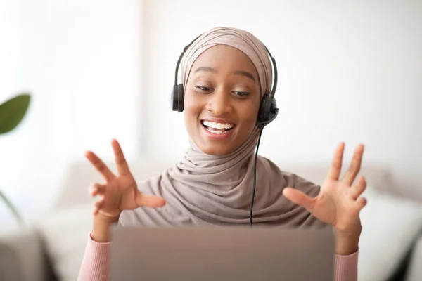 Başörtülü, kulaklık takan çekici Müslüman kadın evde dizüstü bilgisayarla iletişim kuruyor. — Stok fotoğraf