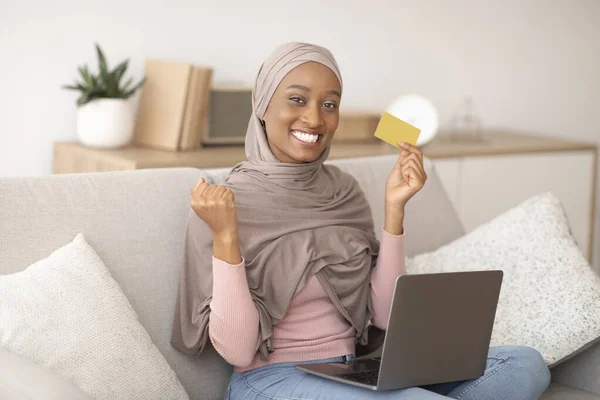 Boldog fekete nő hidzsáb kezében hitelkártya, így IGEN gesztus, online vásárlás laptop számítógép otthon — Stock Fotó