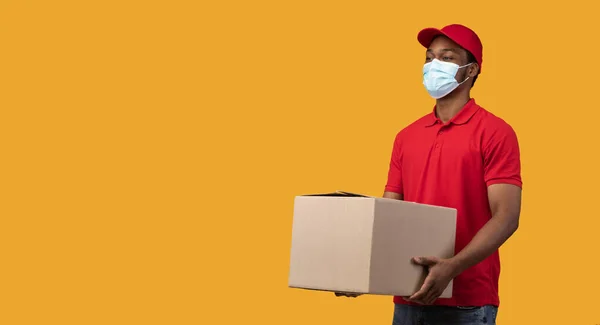 Repartidor negro en máscara médica que sostiene la caja de cartón — Foto de Stock
