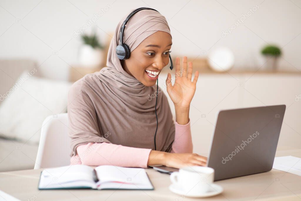 Teleconference. Happy black woman in hijab having video call on laptop computer, talking to coworkers, waving at camera