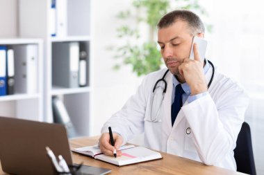 Doktor hasta ile akıllı telefonda konuşuyor ve notlar yazıyor.