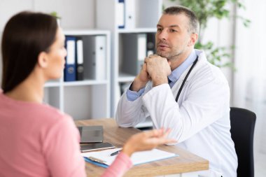 Erkek deneyimli doktor kadın hastasıyla konuşuyor.