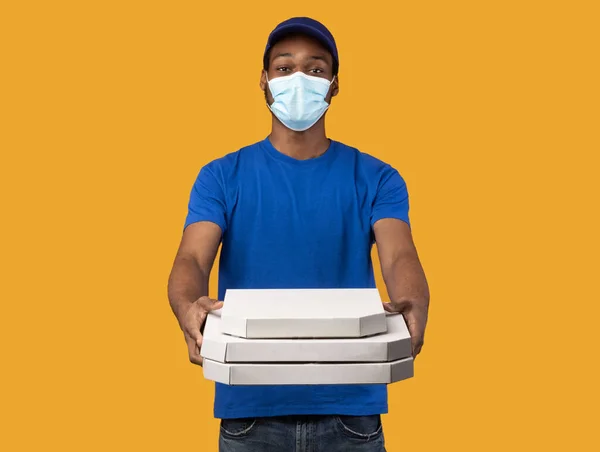 Repartidor negro en máscara médica sosteniendo cajas de pizza —  Fotos de Stock