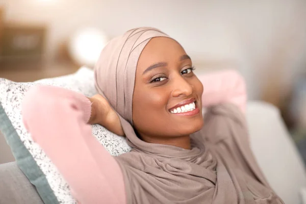 Week-end paisible matin à la maison. Heureuse dame noire en hijab se détendre sur un canapé confortable à l'intérieur — Photo