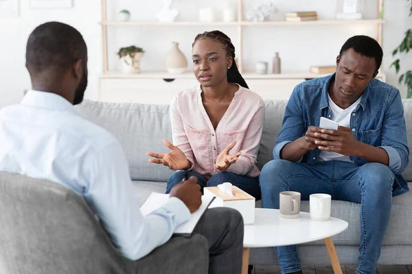 Mulher negra descontente culpando marido na consulta de psicólogo, reclamando sobre o vício em smartphones — Fotografia de Stock