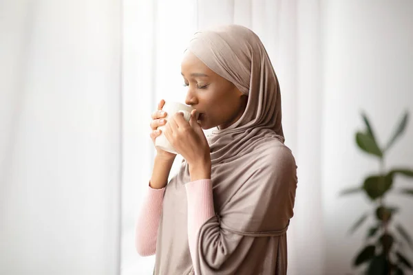 Giovane donna afroamericana in hijab avendo mattina pigra con caffè aromatico a casa, bere bevande calde al chiuso — Foto Stock