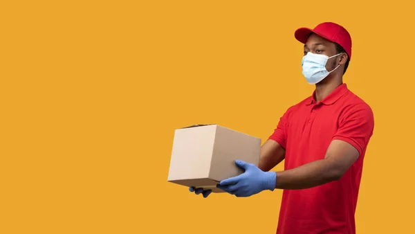 Czarny dostawca w masce medycznej i rękawiczki dając pudełko — Zdjęcie stockowe