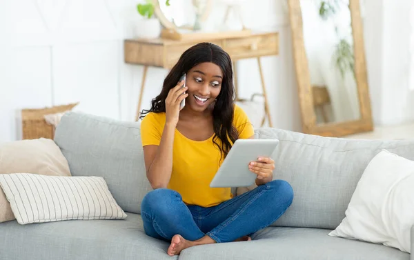 Υπέροχη μαύρη γυναίκα περιήγηση web στον υπολογιστή tablet και μιλώντας στο κινητό τηλέφωνο στο σπίτι, πανόραμα — Φωτογραφία Αρχείου