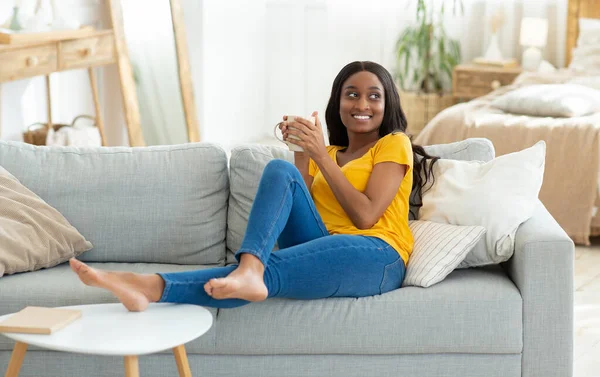 Υπέροχη νεαρή μαύρη γυναίκα που κάνει διάλειμμα για καφέ σε άνετο καναπέ στο σπίτι, αντίγραφο χώρου — Φωτογραφία Αρχείου