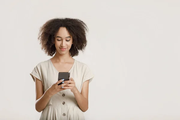 Aranyos nyugodt afro-amerikai Y-generációs nő gépelés okostelefonon, sms üzenet és mosolygós — Stock Fotó