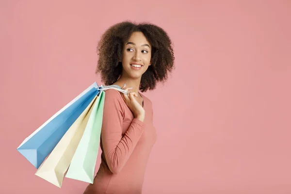 Веселая молодая африканская американка держит цветные сумки, идет вперед и оглядывается назад на пустое пространство — стоковое фото